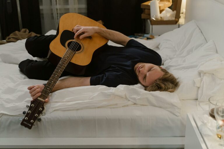 A man lies on a bed playing an acoustic guitar, capturing a moment of solitude and relaxation.