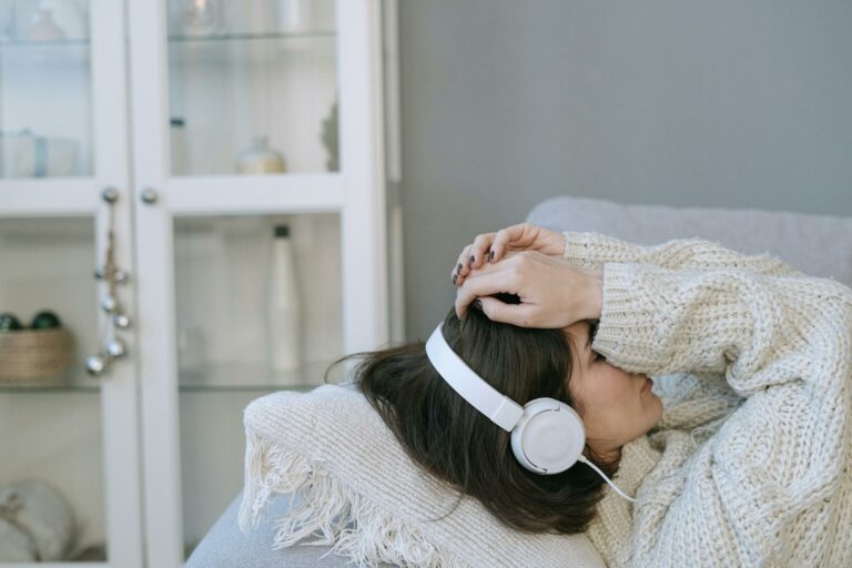 Woman in cozy sweater wearing headphones while lying down indoors, conveying relaxation and comfort.